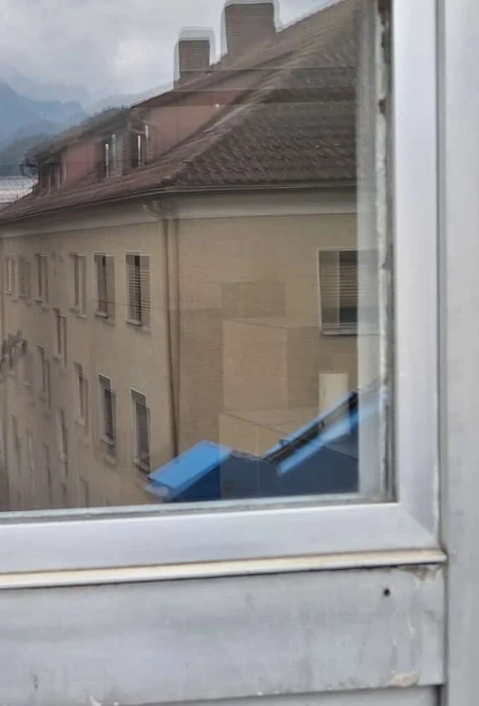 Dasselbe Bürofenster nach der Glasreinigung, das Nachbarhaus samt Kaminen und Bergen dahinter ist gestochen scharf zu sehen