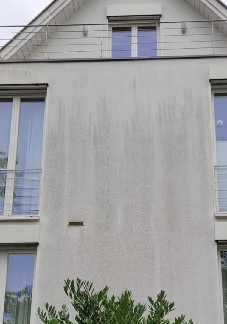 Weiße Hausfassade mit dunklen Schmutzstreifen unter dem Dachvorsprung