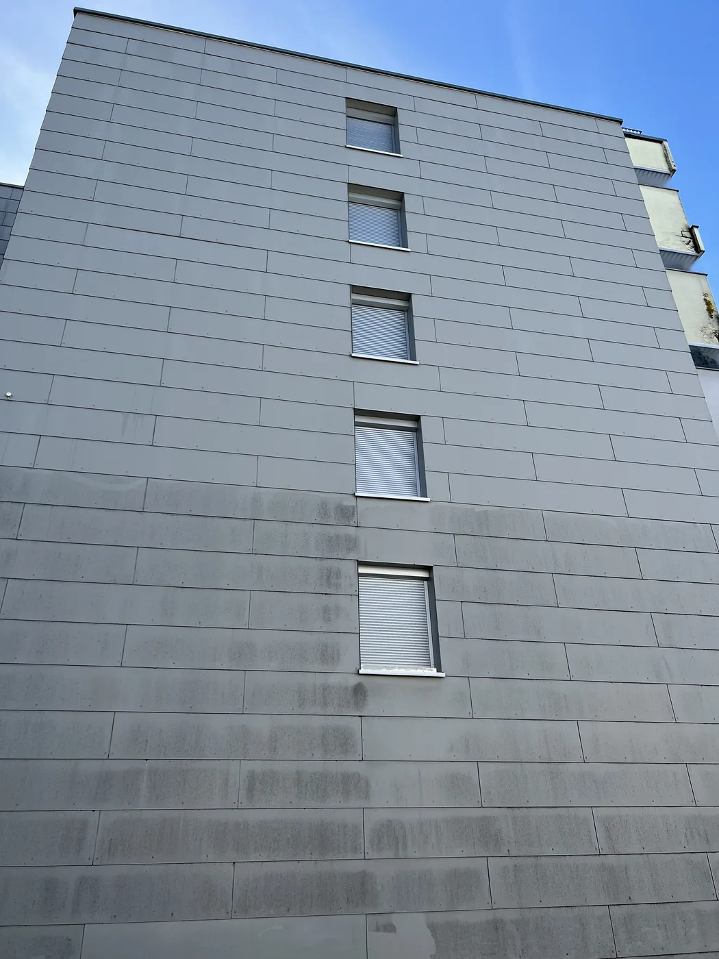 Mehrgeschossige Fassade aus Faserzementplatten, obere Hälfte gereinigt, untere noch verschmutzt