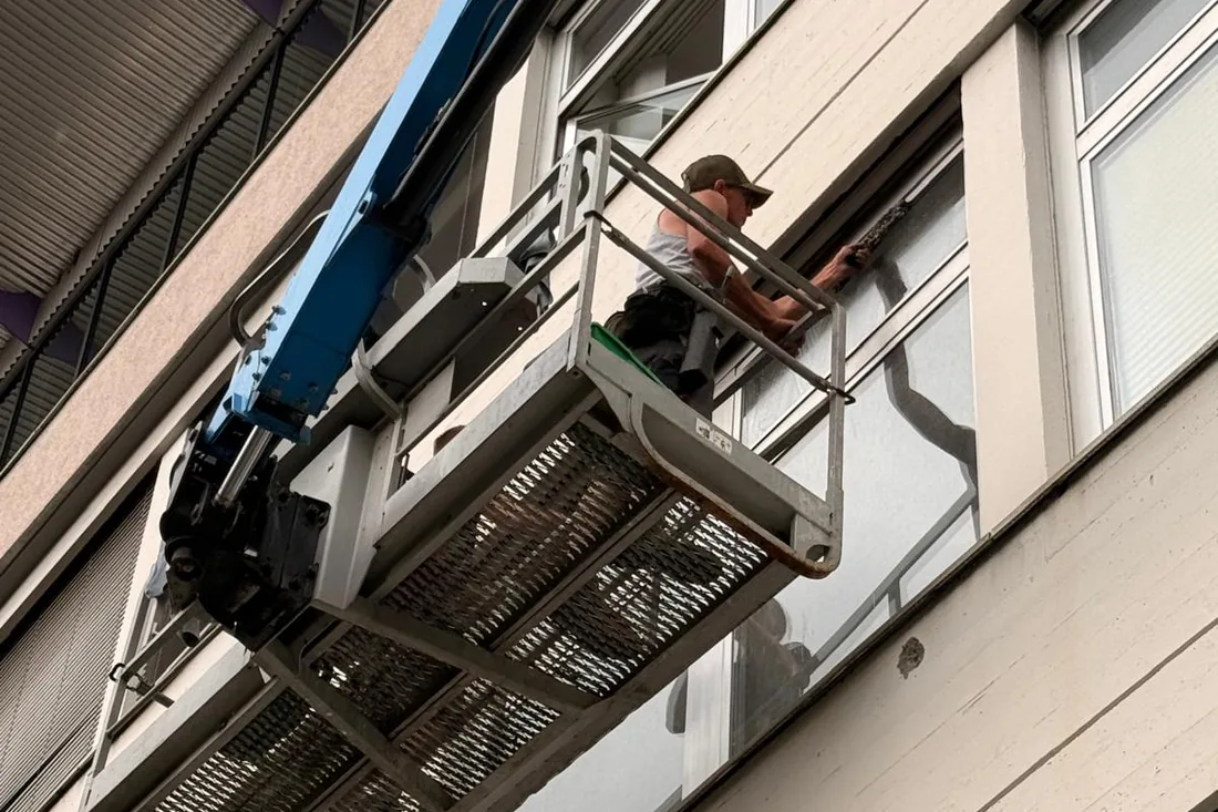 Gebäudereiniger im Korb eines Hubsteigers wäscht die Fenster eines Bürogebäudes im zweiten Obergeschoss ein