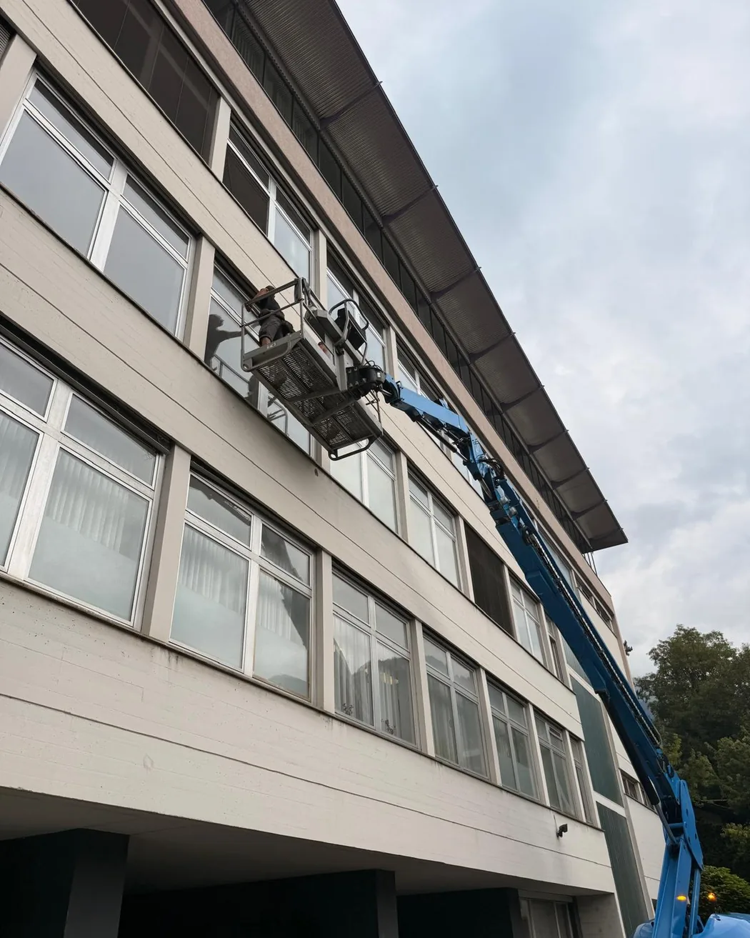 Hubsteiger vor einem viergeschossigen Bürogebäude, der Arbeitskorb steht am oberen Fensterband