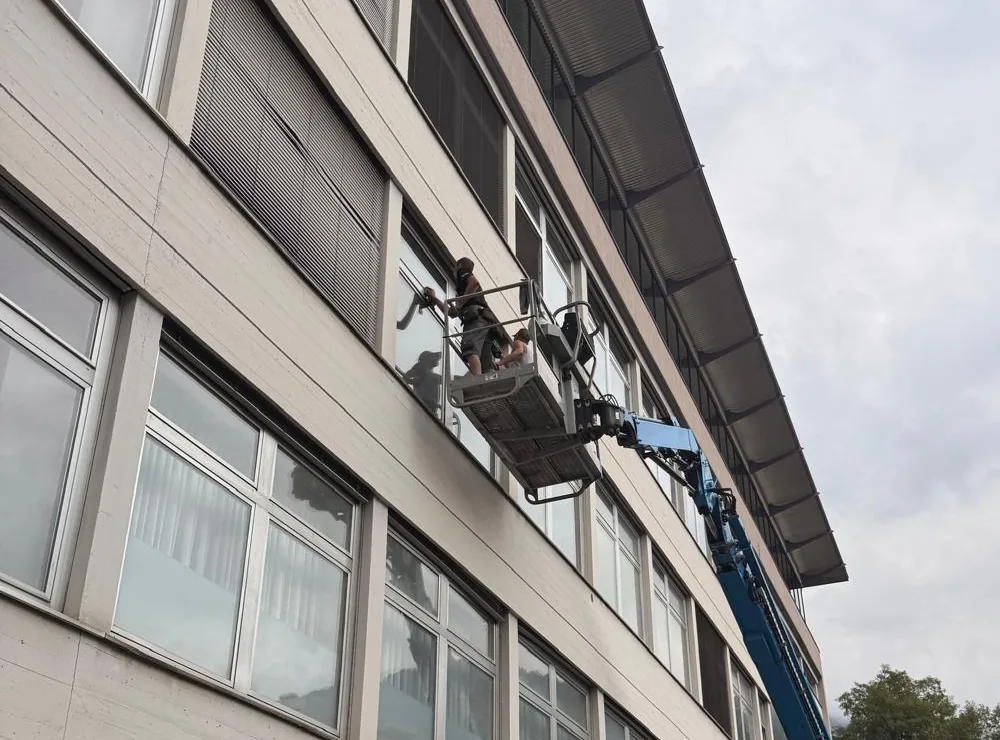 Hubsteiger mit zwei Gebäudereinigern im Arbeitskorb an der Fensterfront eines mehrgeschossigen Bürogebäudes
