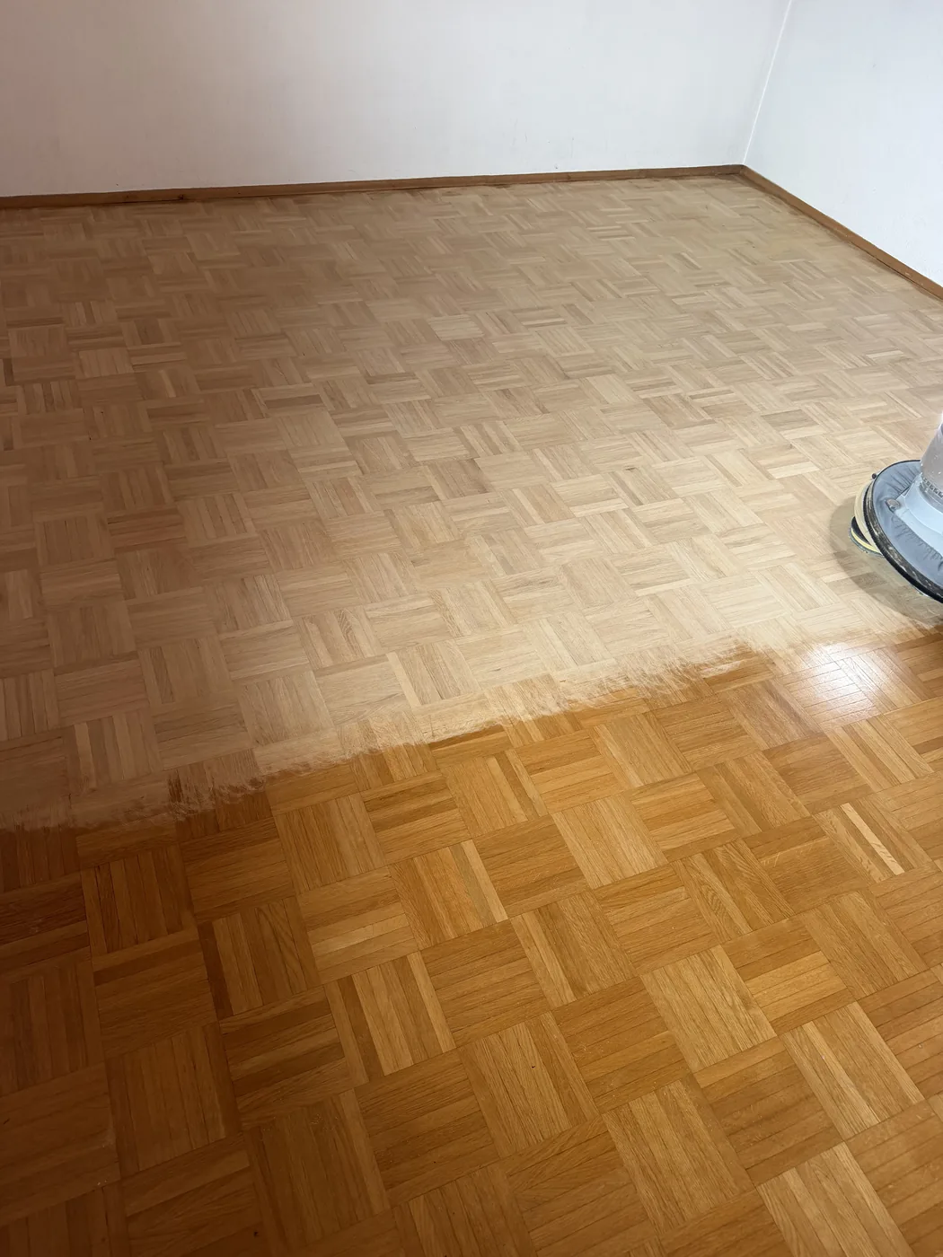 Mosaikparkett während des Schleifens: die bereits bearbeitete Fläche ist hell und matt, der alte Boden daneben dunkelgelb und glänzend