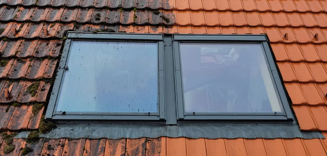 Ziegeldach mit zwei Dachfenstern, links noch bemoost und dunkel, rechts frisch gereinigt und kräftig rot
