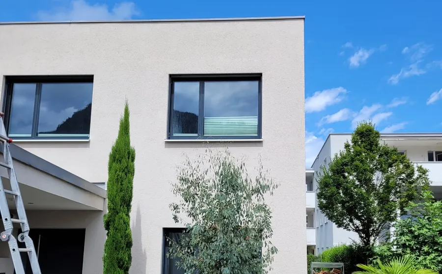 Frisch gereinigte helle Putzfassade eines Wohnhauses mit angelehnter Leiter bei Sonnenschein
